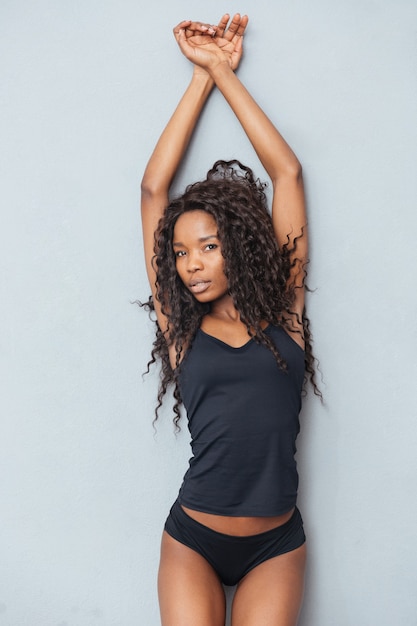 Affascinante donna afro in panno sexy in posa sul muro grigio