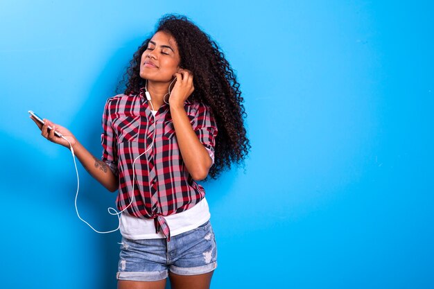 Charming amazing afro american young woman, dancing while listening to music in headphones on her mobile phone.  