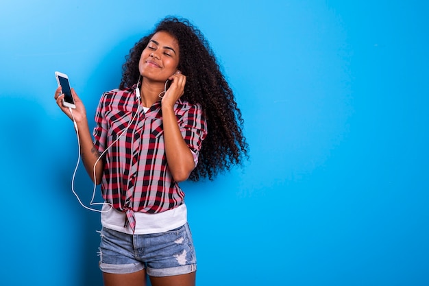 Charming amazing afro american young woman, dancing while listening to music in headphones on her mobile phone.  