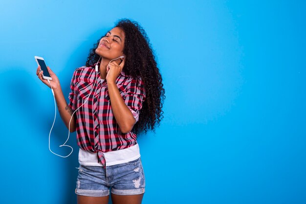 Charming amazing afro american young woman, dancing while listening to music in headphones on her mobile phone