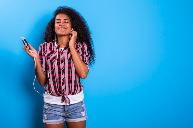 Charming amazing afro american young woman, dancing while listening to music in headphones on her mobile phone