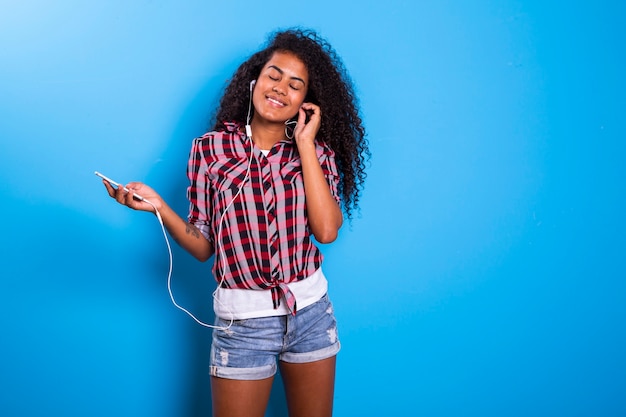 Charming amazing afro american young woman, dancing while listening to music in headphones on her mobile phone.  