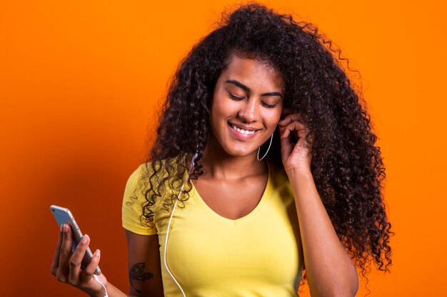 Charming amazing afro american young woman, dancing while listening to music in headphones on her mobile phone.