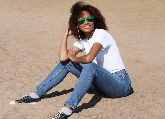 Charming amazing afro american young woman in sunglasses listening to music in headphones on her mobile phone