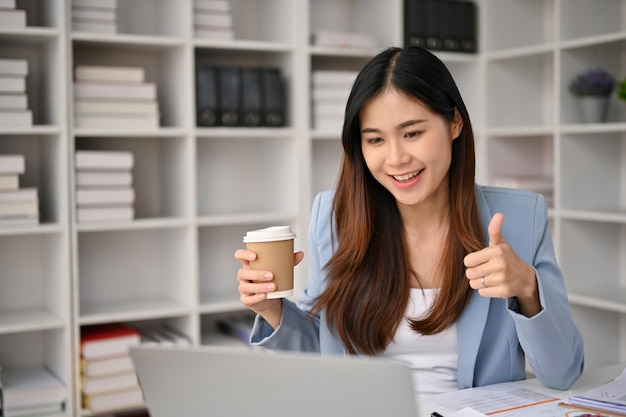 Charming Asian businesswoman giving thumb up to her workers during an online meeting