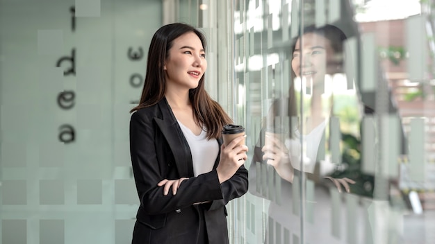 Charming Asian businesswoman standing  holding coffee mug at the office.