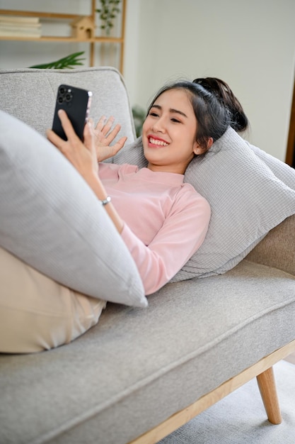 Charming Asian female talking with her friends on the phone while relaxing on the sofa