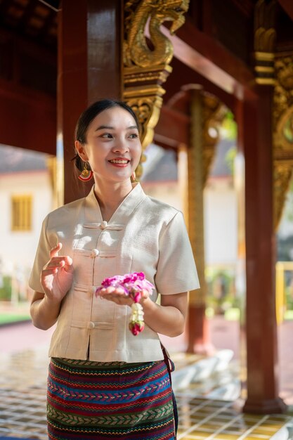 Photo a charming asian thai woman in a traditional thailanna dress is in a temple making a merit