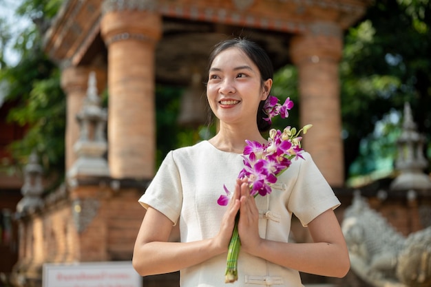 魅力 的 な アジア 人 の 女性 が 寺院 の 外 で 祈り の 姿勢 で 花 を 持っ て 立っ て いる