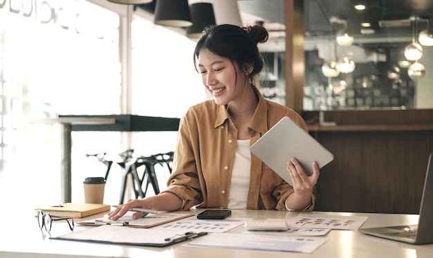 魅力的なアジアの女性は、officexAでタブレットとポイントグラフを持って立っている笑顔で