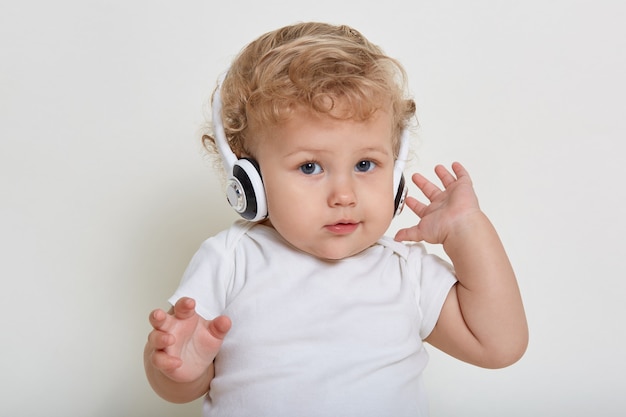 Charming baby boy with beautiful eyes posing with headphones, listening to music, isolated on white space