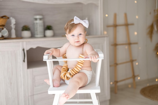 Charming baby girl in diapers sitting in a high chair in the bright kitchen of the house the first lure