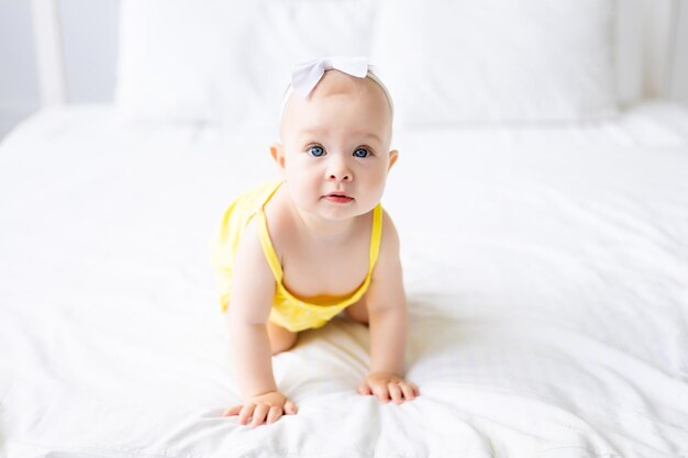 Charming baby girl in a white sunny bedroom A newborn baby is resting in bed Textiles and bedding for children Family morning at home A newborn baby is sitting on the bed after sleeping