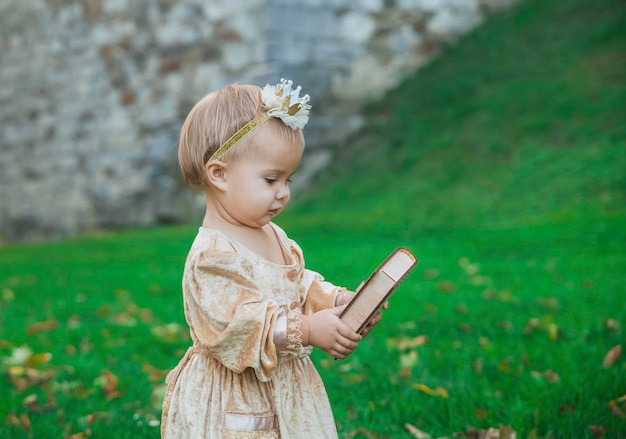 очаровательная малышка в костюме принцессы с короной на голове несет деревянную коробку