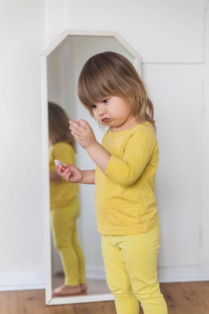 Il bambino affascinante esamina scetticamente un gingillo vicino allo specchio