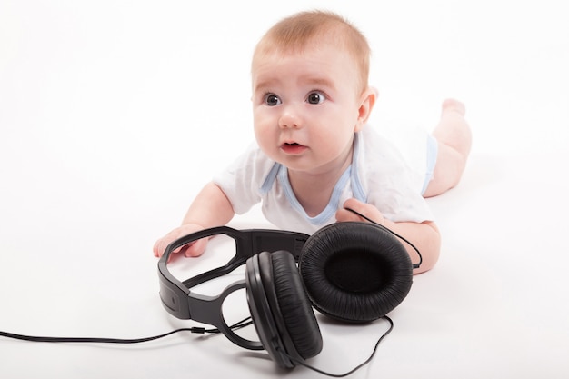 Charming baby on a white background with headphones listening to