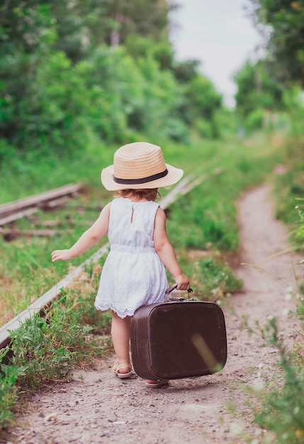 写真 スーツケースを持ったチャーミングな赤ちゃんが鉄道に沿って歩く