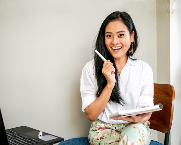 Charming beautiful freelancer smiling face with creative idea holding a pen and note book 