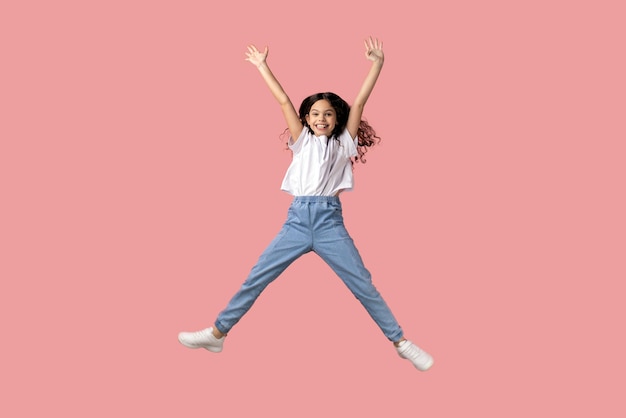 Photo charming beautiful little girl jumping in air and raised arms expressing excitement having fun