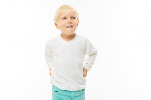 charming blond boy in a white t-shirt thinking on a white wall