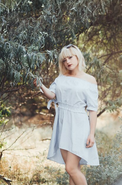 Charming blonde girl with glasses on the head,on a background of green trees at sunset