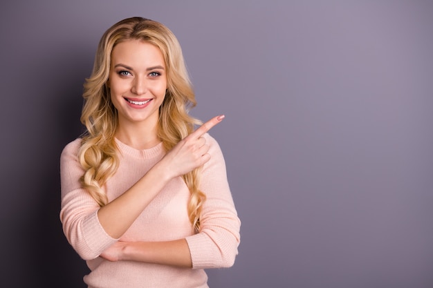 Affascinante donna bionda in maglione rosa in posa contro il muro viola