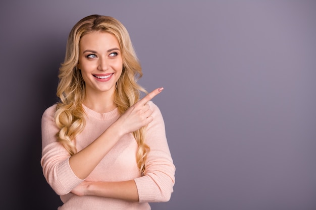 Affascinante donna bionda in maglione rosa in posa contro il muro viola