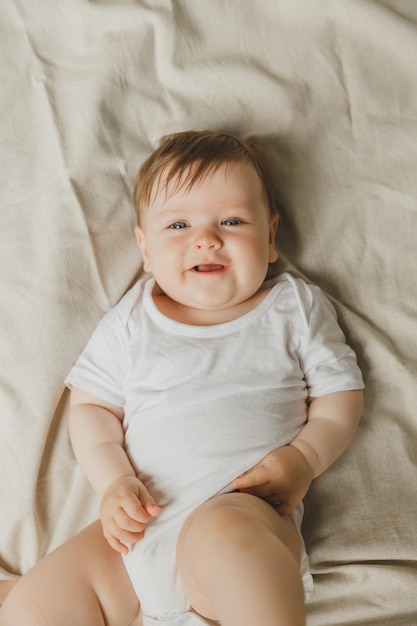멋진 파란 눈의 6 개월 된 아기가 색 바디슈트를 입고 침대에 누워 있습니다.
