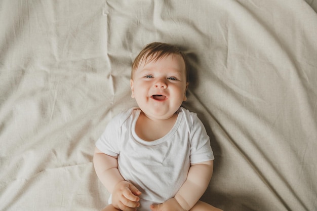 白いボディスーツを着てベッドに横たわっている魅力的な青い眼の6ヶ月の赤ちゃん