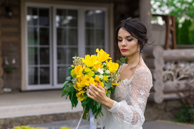 魅力的な花嫁は結婚式の花束を保ち、庭でポーズをとる