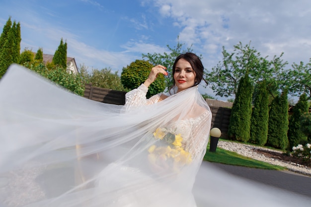 The charming bride keeps a wedding bouquet and sitting on the yard