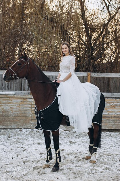 A charming bride rides a horse on a ranch in winter