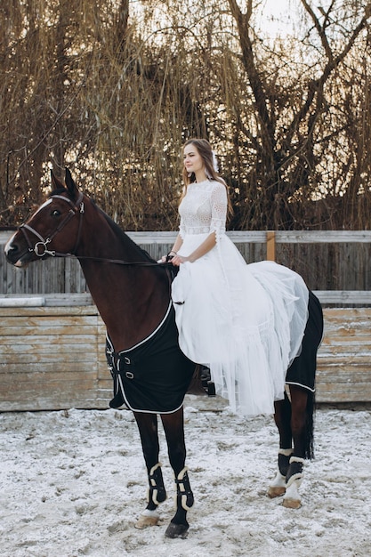 魅力的な花嫁が冬の牧場で馬に乗る