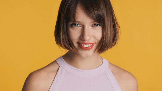 Charming brunette girl with bob hair and red lips happily looking in camera over colorful background