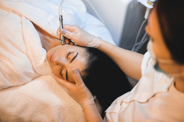 Charming  brunette is having a facial spa procedure while lying with closed eyes