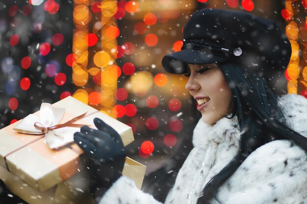 Charming brunette woman receiving gift at the holiday fair during snowfall. Empty space