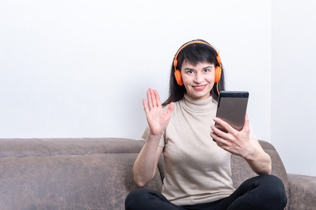 Charming brunette woman wearing orange headphones having a video call and showing a hello or bye gesture