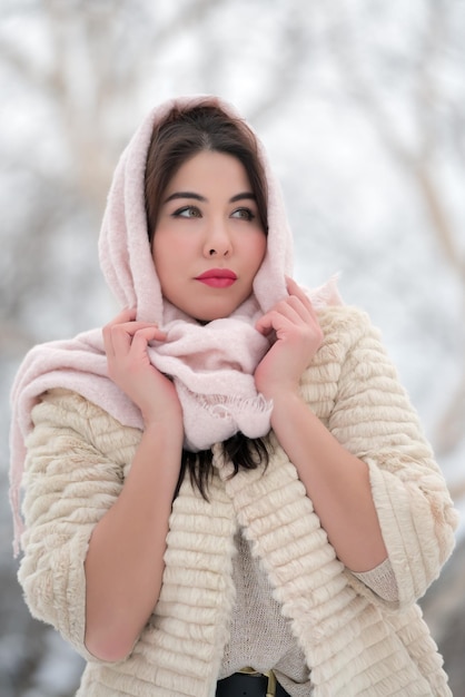 Charming brunette young woman dressed in white threequarter sleeve fur coat and light pink scarf on head