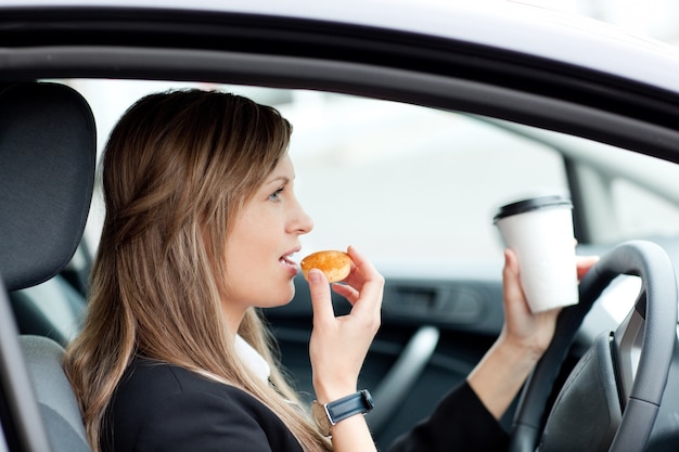 運転中の飲み物のカップを飲みながら魅力的な実業家