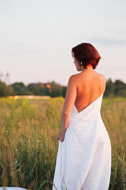 Charming caucasian woman in a field at sunset in summer back view