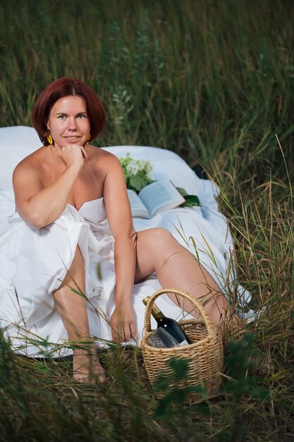 Photo charming caucasian woman sitting in the white bed in a field at sunset in summer