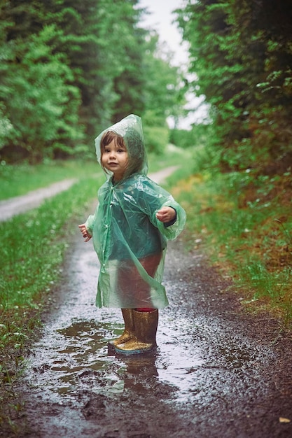 Photo charming child in a raincoat in the evening forest in denmark