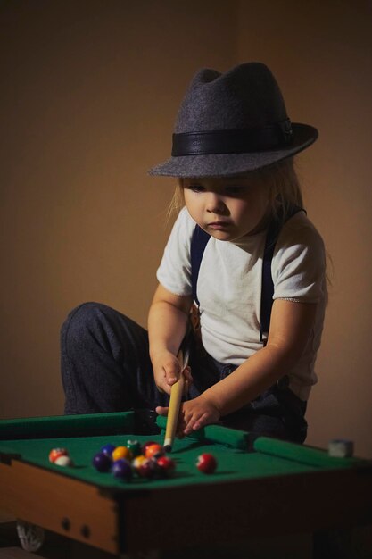 Photo charming child in retro clothes playing toy billiards