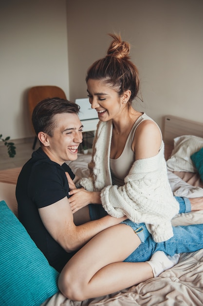 Charming couple are playing in bed embracing and laughing in the weekend