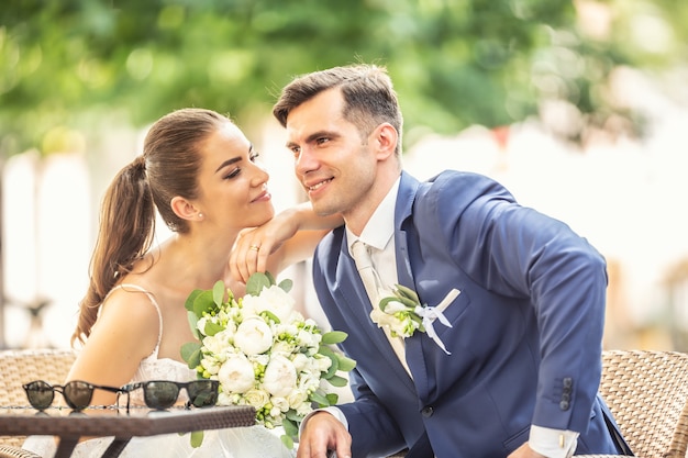 Charming couple sitting in town after a wedding, holdind an amazing bouquet and thinnking about future life.