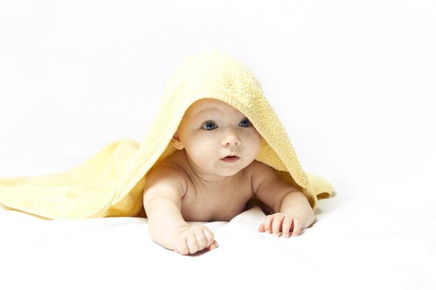 Charming, cute, happy baby girl with blue eyes in a yellow towel on a white background.