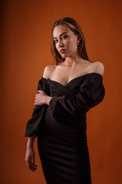 Charming elegant fashion model wearing black dress with deep neckline on orange