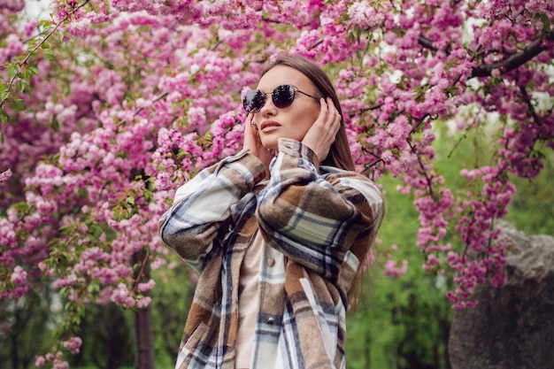 Foto affascinante donna alla moda nel parco fiorito di sakura