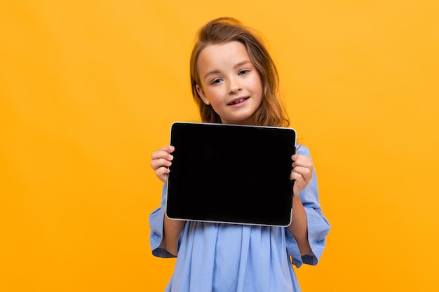 Charming girl in a dress shows a tablet display on a bright yellow background