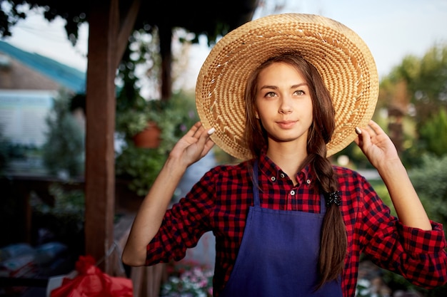 Charming girl gardener in a straw hat is standing in the wonderful garden on a sunny day. .